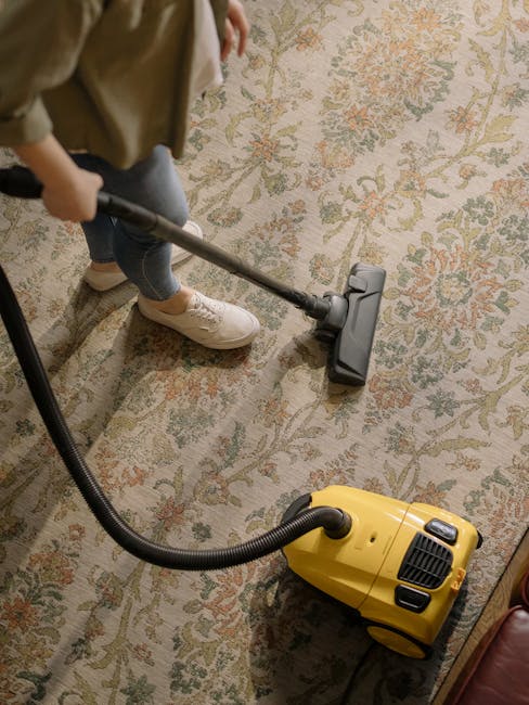 Close-up view of a wet vacuum cleaner with a clear cylindrical dust container filled with moisture and debris, connected to a flexible, black-and-white patterned hose attached to a cleaning floor nozz