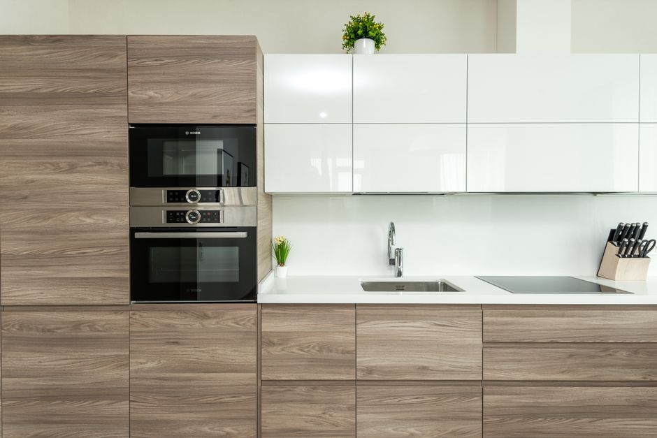 A person wearing a black long-sleeve shirt is placing a tray of cooked rice into a modern, stainless steel oven for surface cleaning and deep sanitisation. The oven is built into a dark grey kitchen w